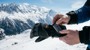 A close-up view of a slim rechargeable lithium-ion battery being inserted into the cuff pocket of a heated ski glove.