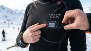 User adjusting temperature controls on a heated base layer shirt for skiing during a cold day.